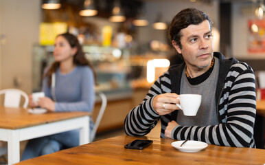 Lonely man drinking coffee and looking at mobile phone screen. Waiting for meeting
