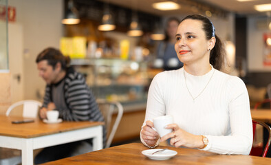 Woman in white blouse is sitting in cafe with a cup of hot strong coffee