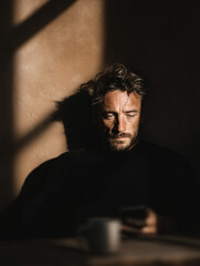 Urban Leisure Calm Casual Man Facial Hair Natural Light Shadow Relaxed Mobile Coffee Cup Focus Technology Stylish Soft Mood Alone Warm Expression Concentration Indoors Modern Elegance Simple