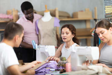 Friendly middle-aged woman talking with man and sewing, other working with mannequin in dressmaking...
