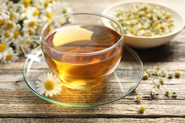 Aromatic tea in glass cup and chamomile flowers on wooden table, closeup