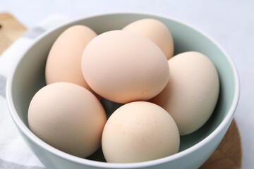 Raw chicken eggs in bowl on white table, closeup