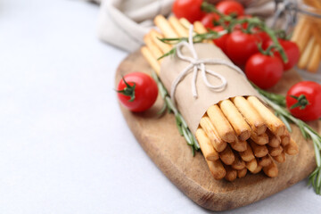 Delicious grissini sticks, rosemary and fresh tomatoes on light table, closeup. Space for text