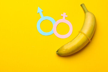 Sex education. Banana with condom, paper female and male gender symbols on yellow background, flat...