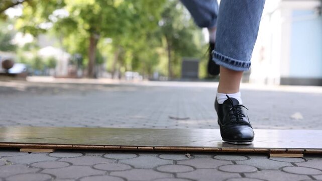 Teenage girl in tap shoes dancing outdoors, closeup. Camera moving down