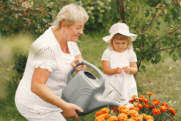 Little girl and her grandmother watering flowers in garden