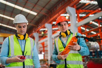 Professional engineer working in metal factory inspecting steel coil rolls, wearing safety gear,...