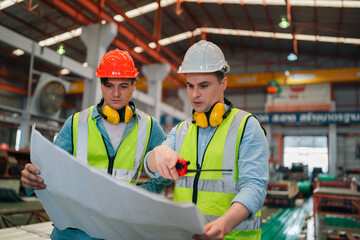Professional engineer working in metal factory inspecting steel coil rolls, wearing safety gear,...