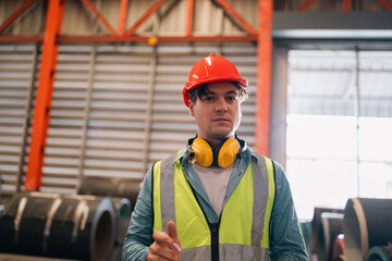 Professional engineer working in metal factory inspecting steel coil rolls, wearing safety gear,...
