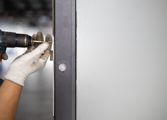 Worker in uniform with screw gun repairing door lock indoors