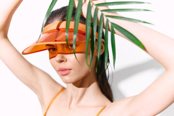 Stylish summer portrait of a woman with orange visor and palm leaves, showcasing vibrant fashion...