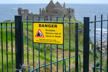 Warning sign indicating danger of rockfalls near cliffside ruins on a coastal landscape