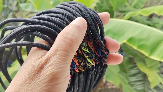 Parachute cord necklace black with multicolor loops in hand on green blurred tree background.