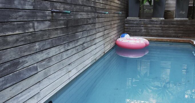 Pink inflatable donut float drifting in backyard pool, with beach ball and potted plants
