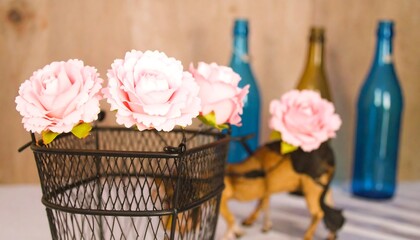 Delicate pink flowers rest in a black wire basket, accented by decorative bottles, creating a charming and rustic display.