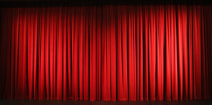 Beautiful full length luxurious traditional red burgandy stage curtains on a theatre stage with dark vignette and spotlighting.