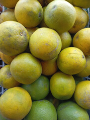 full frame shot of fresh green and yellow oranges piled high in a white basket, showing a variety of ripeness and natural blemishes.