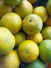  full frame shot of fresh green and yellow oranges piled high in a white basket, showing a variety of ripeness and natural blemishes.