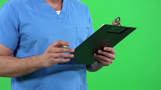 A middle-aged man in a light-blue medical uniform stands in front of a solid green background, expressing a thoughtful or concerned expression.