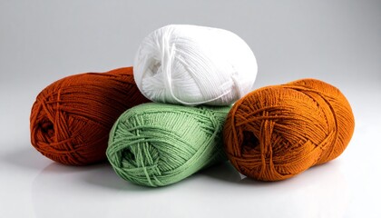A colorful assortment of five yarn balls, including white, green, and two shades of orange, artfully arranged on a light gray surface.