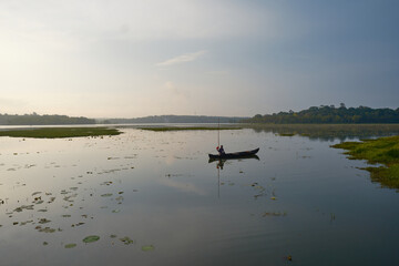 Fishermen in traditional wooden canoes navigate the calm waters of Vellayani Lake in Thiruvananthapuram, Kerala, as the morning sun casts a gentle, ethereal glow. Kerala backwater