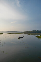 Fishermen in traditional wooden canoes navigate the calm waters of Vellayani Lake in Thiruvananthapuram, Kerala, as the morning sun casts a gentle, ethereal glow. Kerala backwater