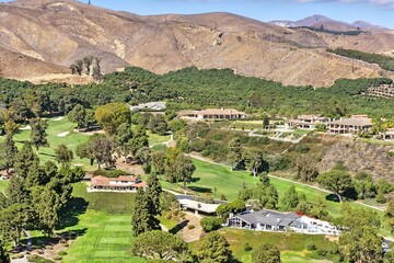 Aerial view of golf course and houses in a sunny landscape.