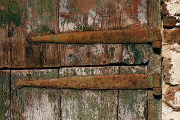 A rustic latch is covered in rust, set against a wooden door with peeling green paint. The texture of the wood and the aged metal creates a visually compelling contrast. 