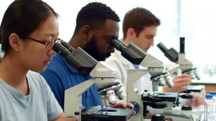 A diverse group of young scientists or students intently focused on their work, using modern microscopes in a brightly lit, professional laboratory setting. - Powered by Adobe