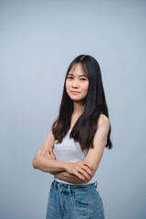 Confident young woman with long black hair wearing a white tank top and blue jeans, standing with...