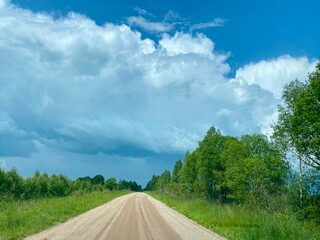 A Scenic Dusty Road Winding Its Way Through a Lush Green Landscape Beneath Dramatic Clouds