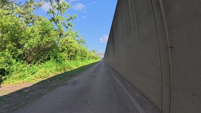 POV cycling on the Riverfront Trail alongside a massive concrete floodwall near the Mississippi River above St. Louis, Missouri - Urban biking scene showing flood protection wall  and unique riverside