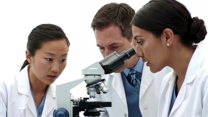A diverse team of male and female scientists in white lab coats collaborating and looking intently into a microscope during a research experiment in a laboratory. - Powered by Adobe