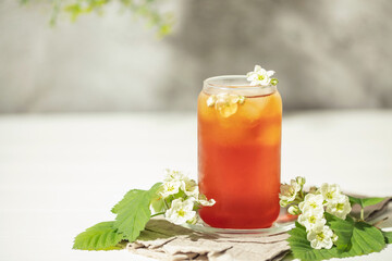 Alternative herbal drink. Hawthorn spring floral iced tea in glass with spring blooming branches  on wooden background
