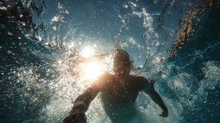 A creative shot of a swimmer, viewed from below the water, with the sunlight filtering down through the surface. The light creates beautiful, dancing patterns.
