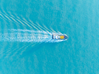 A lone boat moves across the wide blue ocean creating a foamy white wake as it sails calmly on the...