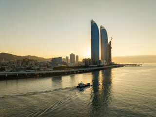 Golden sunrise illuminates the Xiamen China city skyline, featuring modern skyscrapers reflected on...
