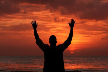 Fototapeta premium Man Surrendering: Silhouette of Man with Raised Hands at Beach Sunset