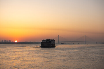 Obraz premium Beautiful sunset creates a warm glow over Yangtze River, highlighting the central building and distant bridge in Ezhou City, Hubei Province, China.