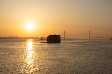 Vast Yangtze River water in Hubei Province, China, reflects the bright sunset as an old fort stands...