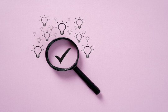 Magnifying glass highlighting check mark among light bulbs on pink background, symbolizing idea selection, solution, creativity, innovation, problem solving, and decision making.