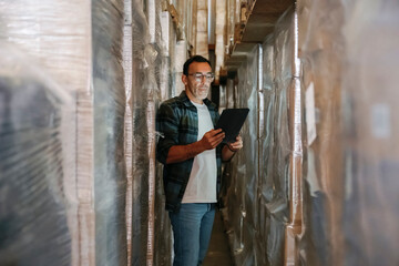 Warehouse manager using digital tablet checking inventory between shelves with goods