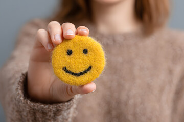 A smiling woman holds a happy face in her hand, symbolizing positive thinking and mental health awareness. This concept promotes the importance of mental health and World Mental Health Day.