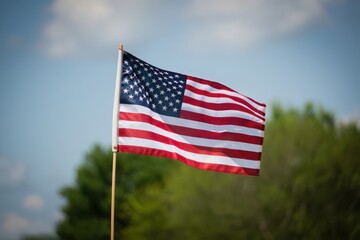 American flag waving proudly against a blue sky with green trees