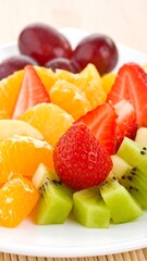 Colorful fruit salad with strawberries, mandarin oranges, kiwi, and grapes arranged artfully on a white plate