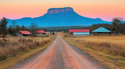 Rural road leading to distant mountain at sunset