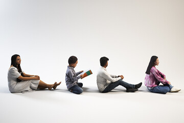 Fototapeta premium Four people sit side by side on the floor against a blank background.