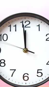4K footage vertical video close-up view wall clock shows the time precisely at 11:59, set against soft pink gradient background. 