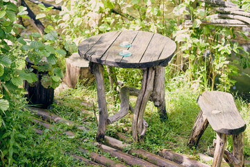 Rustic wooden table and stool surrounded by greenery near a water stream in a serene outdoor setting