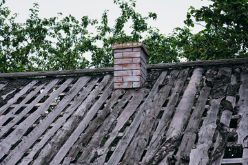Old rickety roof with damaged wood panels and a small brick chimney on an overcast day